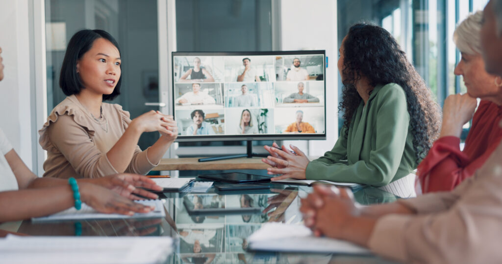 Group of people around a table conducting a hybrid meeting with people on a monitor joining virtually.