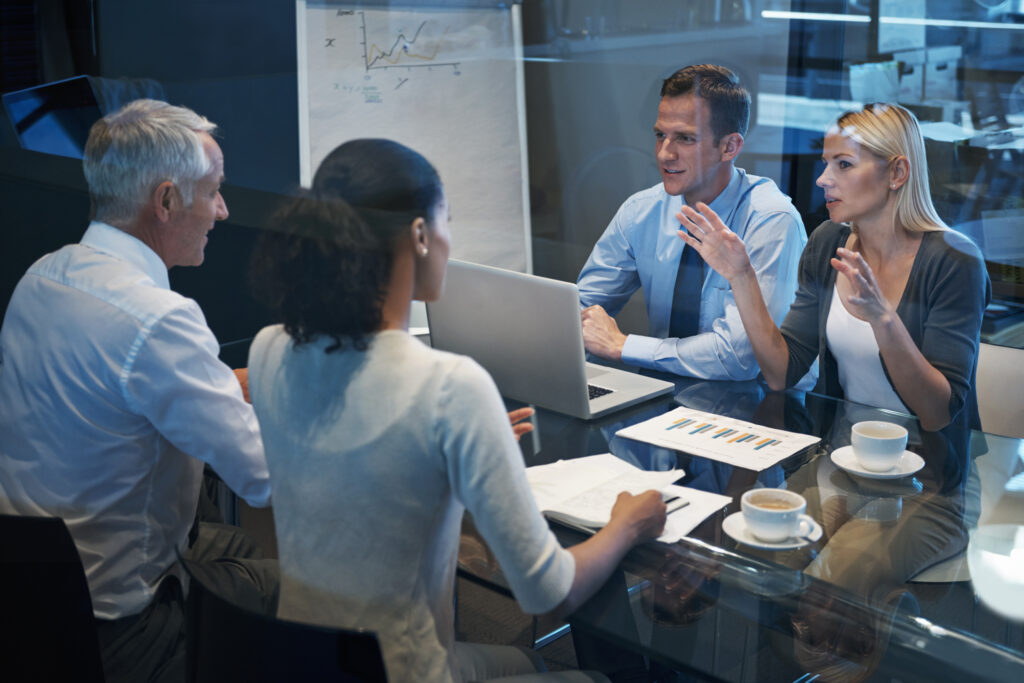Four business professionals seated around a conference table during a workplace meeting and discussion
